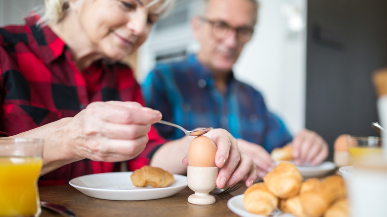 elderly woman cracking boiled egg open