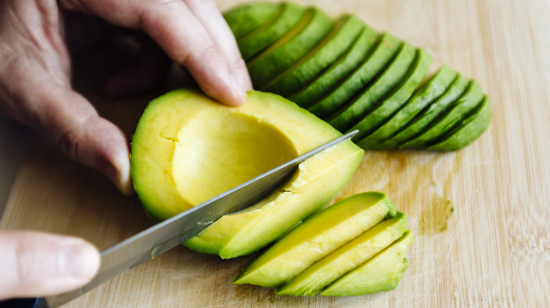 hands cutting avocado on cutting board