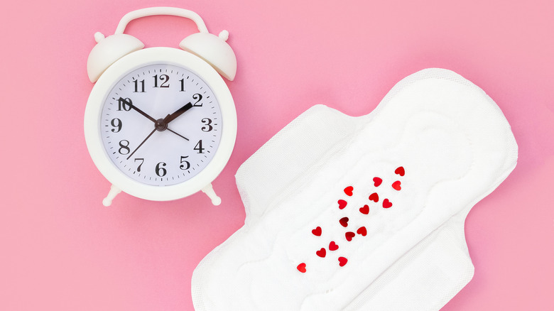 female monthly pad and a white alarm clock on a pink background