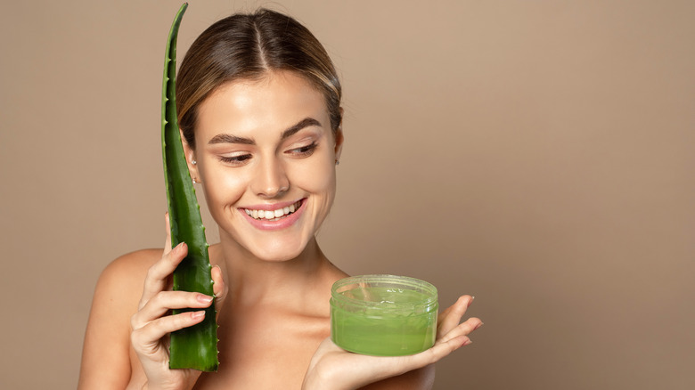 Woman holding aloe vera gel in one hand and an aloe leaf in the other