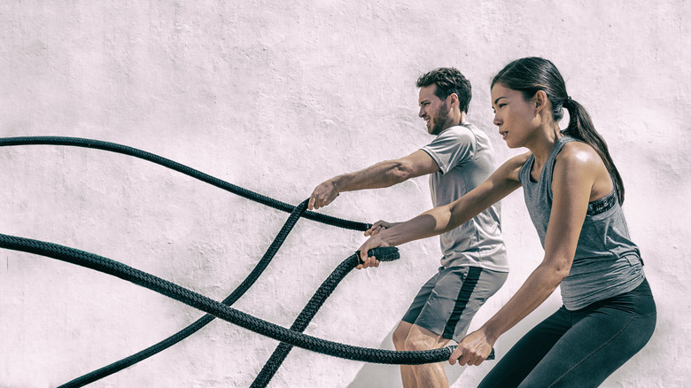 A man and woman using fitness battle ropes. 