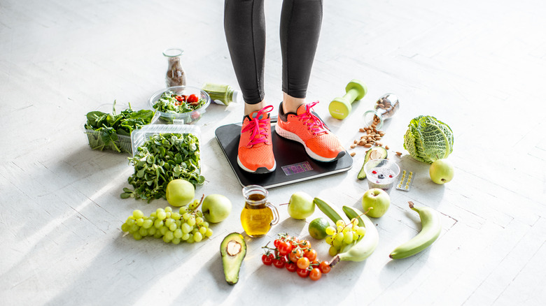Woman on scale in sneakers surrounded by healthy produce.