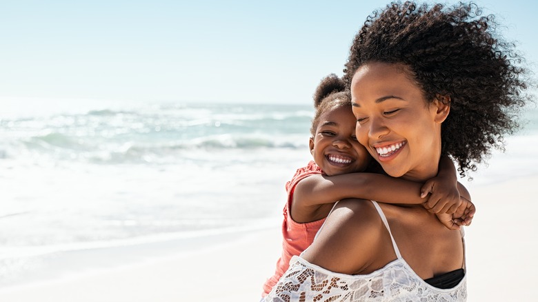 Mom with her daughter on her back, smiling on a beach.