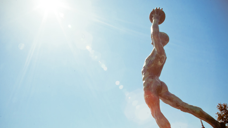 Statue of a nude, ancient athlete raising an exercise ball overhead.