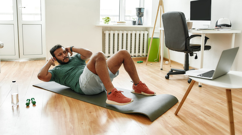 Man doing crunches on a yoga mat with a lap top at home.