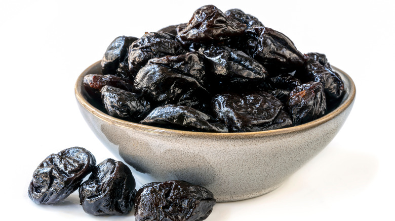 Prunes in a bowl and on table with white background