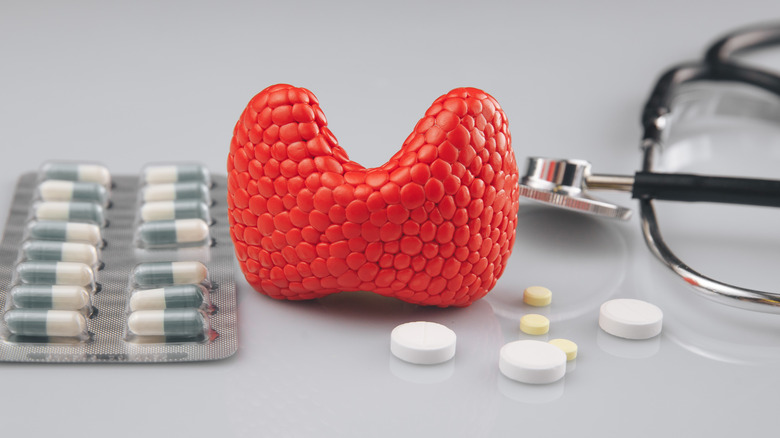 Model of thyroid gland surrounded by pills and stethoscope