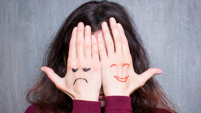 Woman with hands over eyes, each hand representing happy and sad