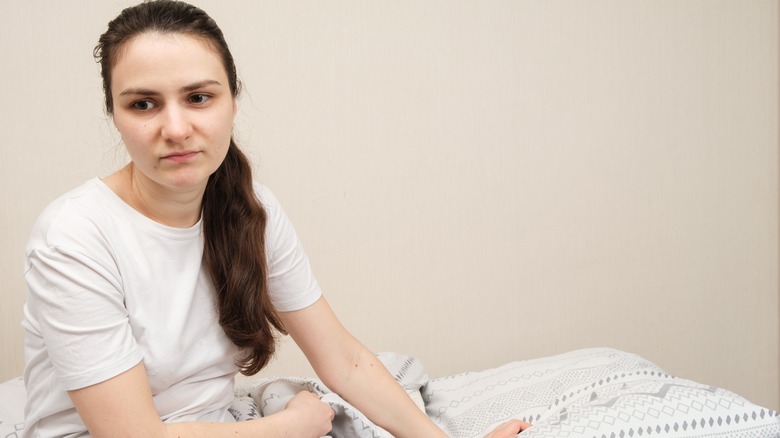 Woman sitting on bed looking unhappy