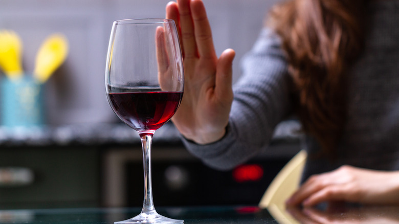 woman holding up hand against glass of red wine