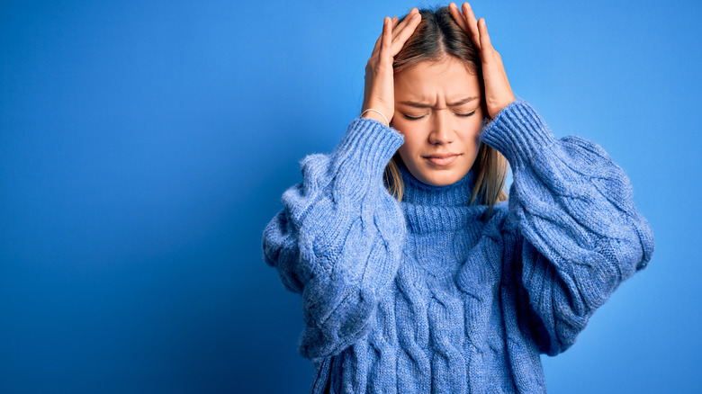 a woman standing in front of a blue background looking stressed with a headache