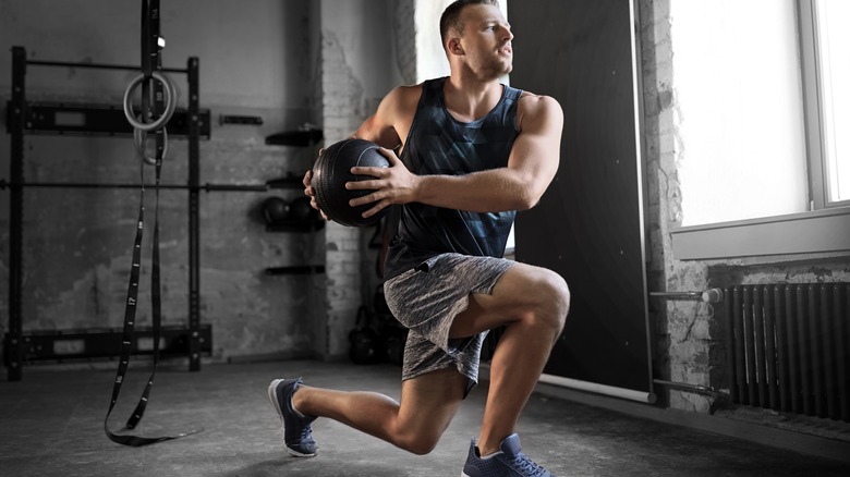 Man holding medicine ball and performing lunge with twist