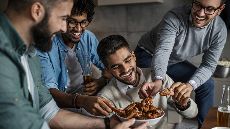 A group of men eating chicken wings from a bowl