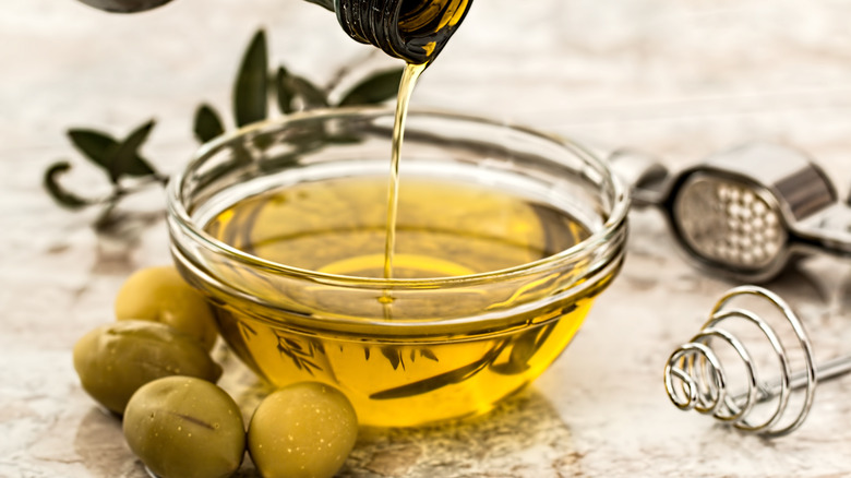 olive oil poured into glass bowl with olives nearby