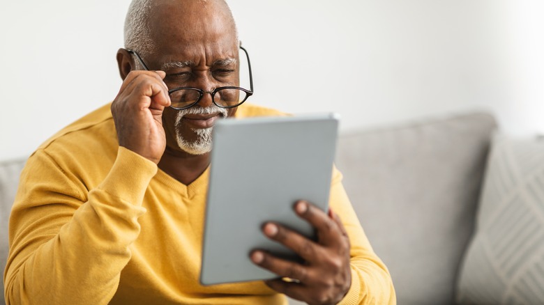 Older man holding glasses and squinting at tablet