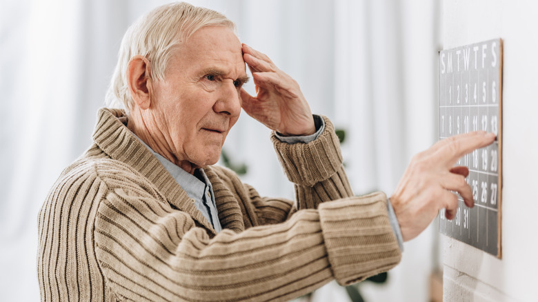 Older man pointing at calendar and holding head