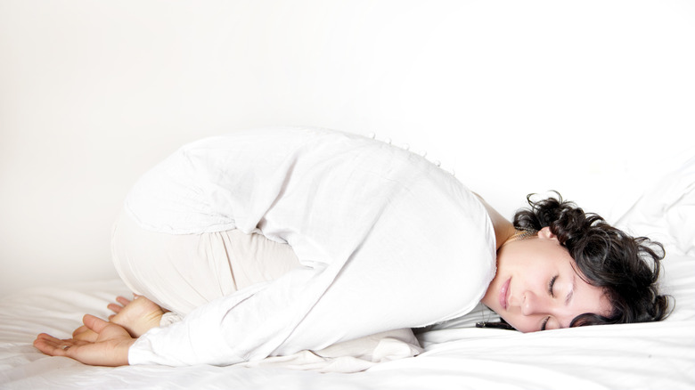 Woman doing child's pose in bed with her eyes closed