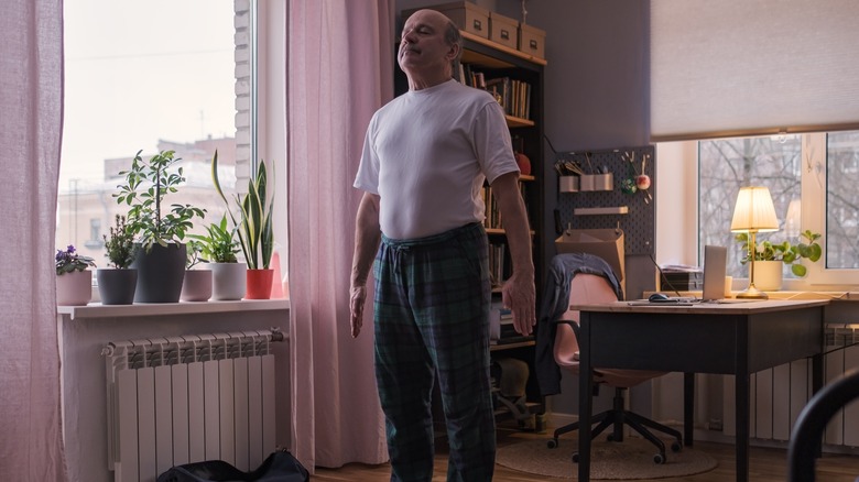 Older man doing Mountain pose on a yoga mat in bedroom