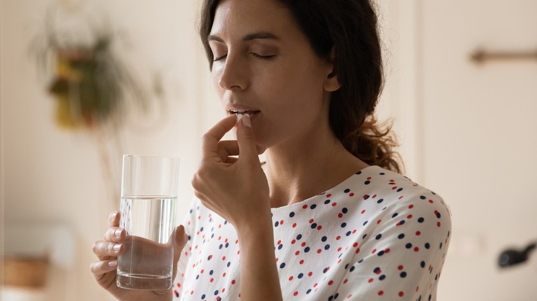 Woman holding glass taking a pill