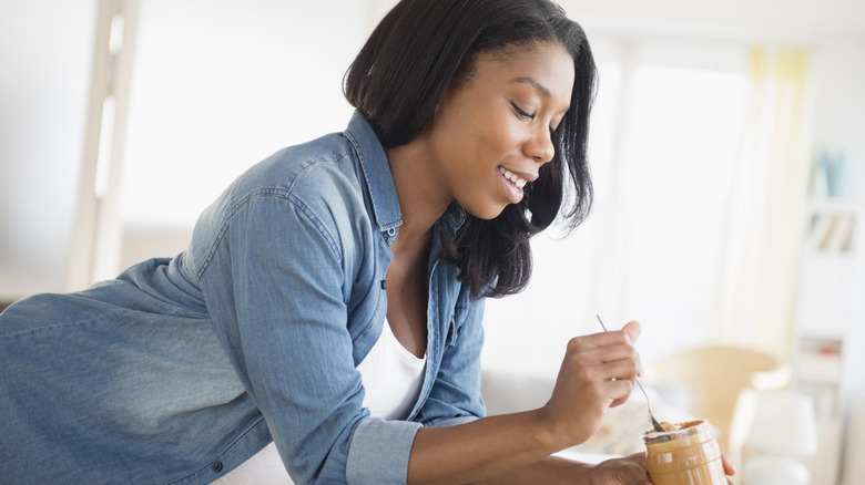 smiling woman eating peanut butter out of jar