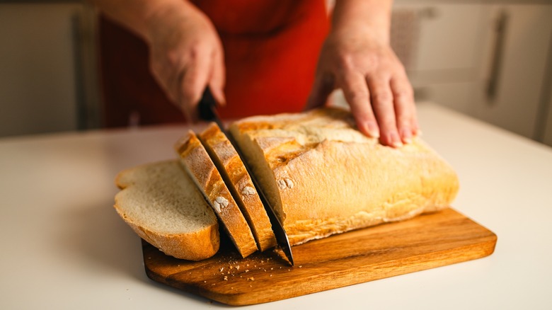 woman slicing fresh bread on cutting board