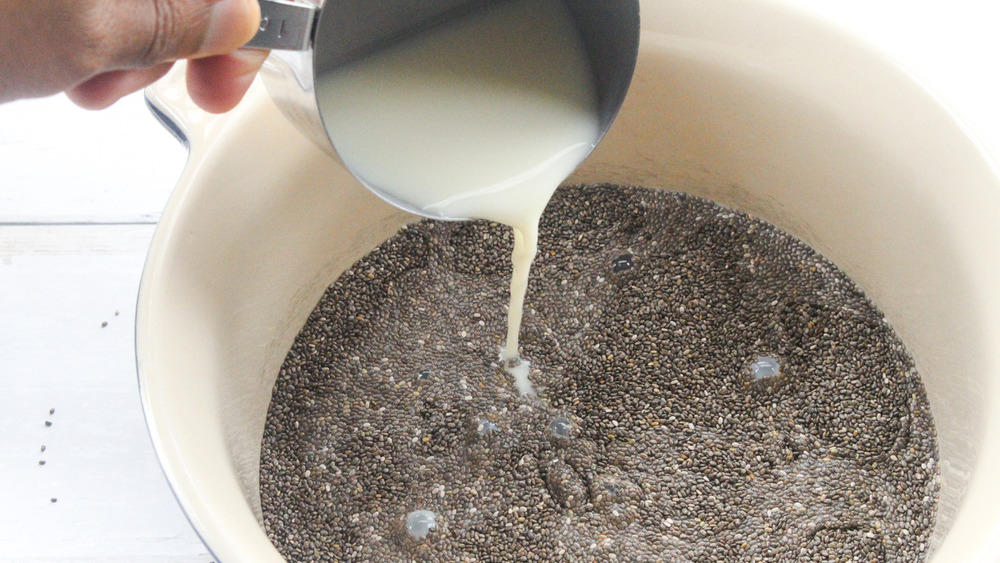 Cup of milk being poured into bowl of chia seeds