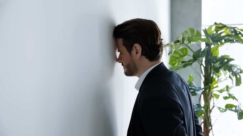 man pressing forehead to wall