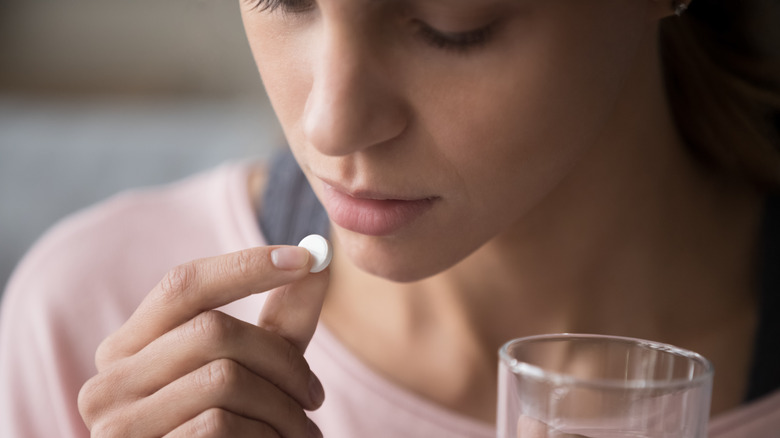 A woman with a glass of water in one hand and an aspirin in the other