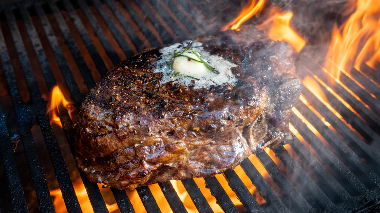 rib-eye beef steak with dollop of butter on flaming grill
