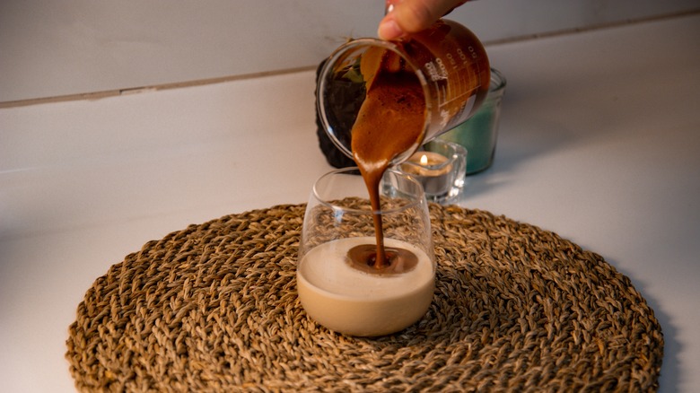 person pouring coffee into a coffee cup with milk