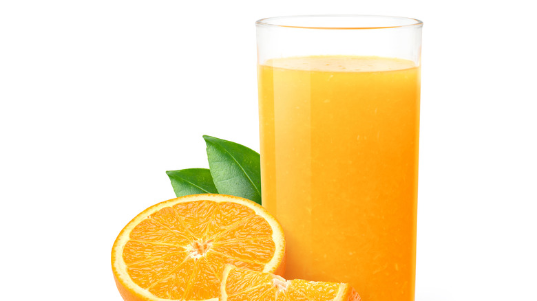 a glass of orange juice with a sliced and halved orange by its side