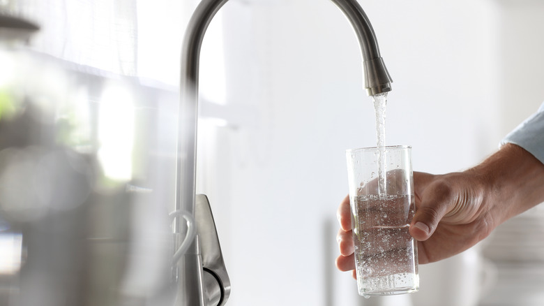 person filling cup of water up from tap