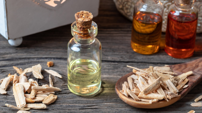Bottle of essential oil next to cedarwood chips and a wooden spoon