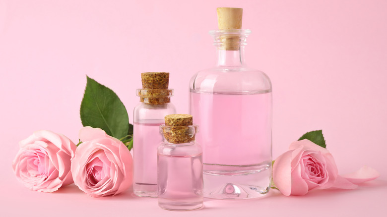 Three bottles of essential oil by pink roses against a pink background