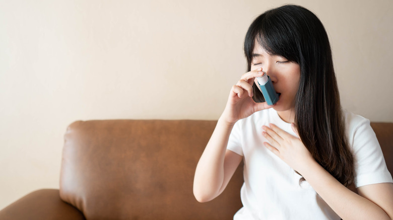 Woman sitting on a brown couch using an inhaler