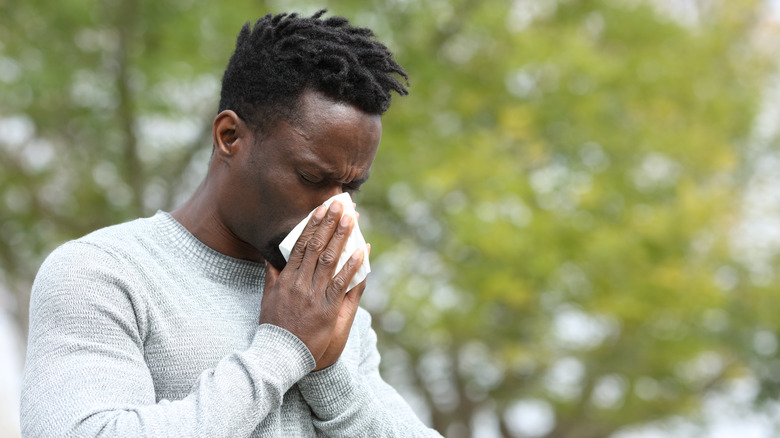 Man in a long-sleeved shirt blowing his nose