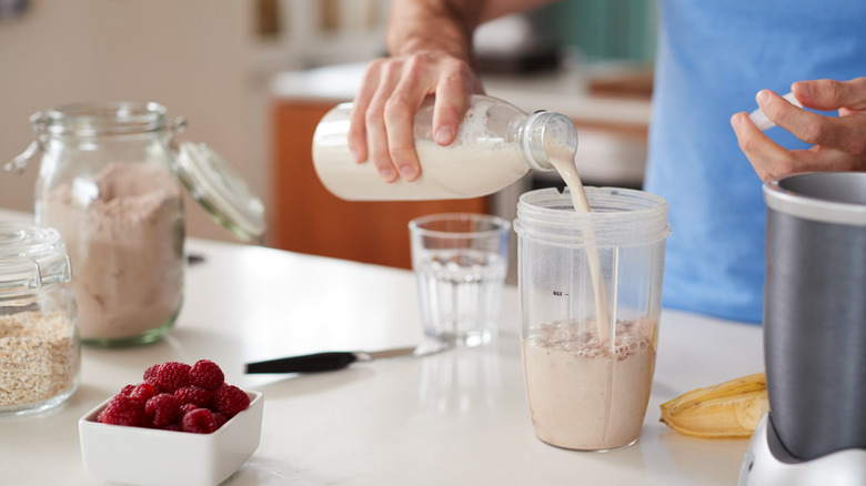 person pouring a protein shake into glass