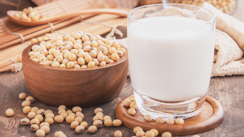 A glass of soy milk next to bowl of soy beans