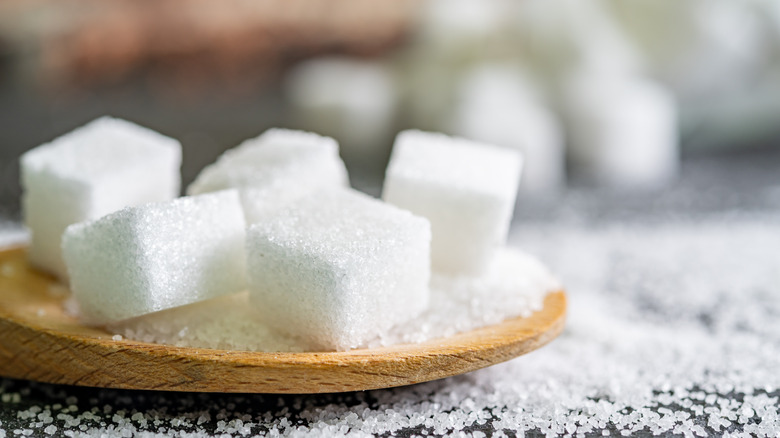 Sugar cubes on a wooden board on top of granulated sugar