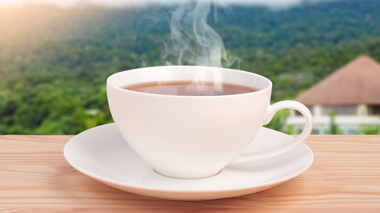 cup of steaming tea on wooden table with mountains in background