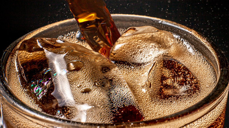 Close up of cola being poured into a glass that has ice cubes in it