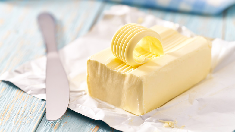 Butter next to a butter knife on a white wrapper on top of a painted wooden surface