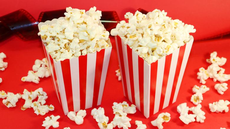 Two striped containers of popcorn next to film and more popcorn against a red surface