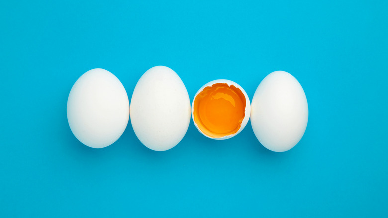 Three whole white eggs and one broken white egg with the yolk showing against a blue background