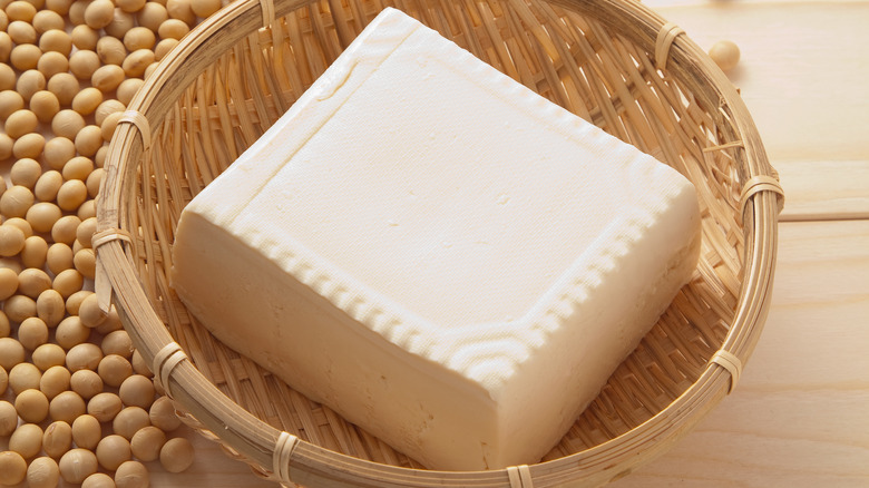 Overhead close up shot of a block of tofu in a basket next to soybeans