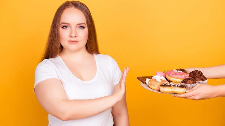 young woman saying no to a plate of junk food