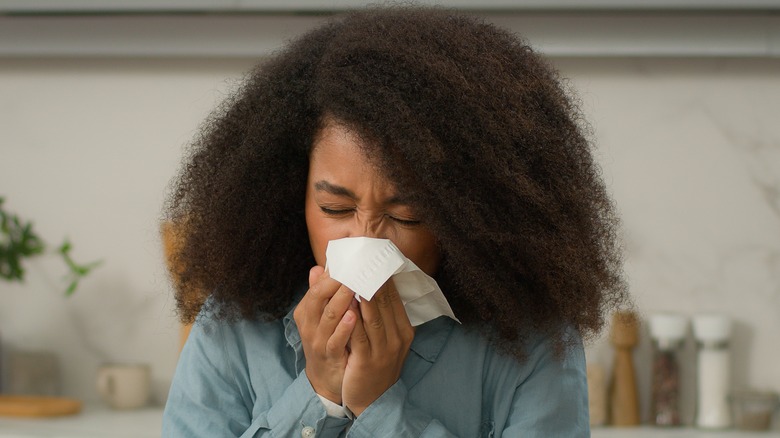 Young woman sneezing in her kitchen