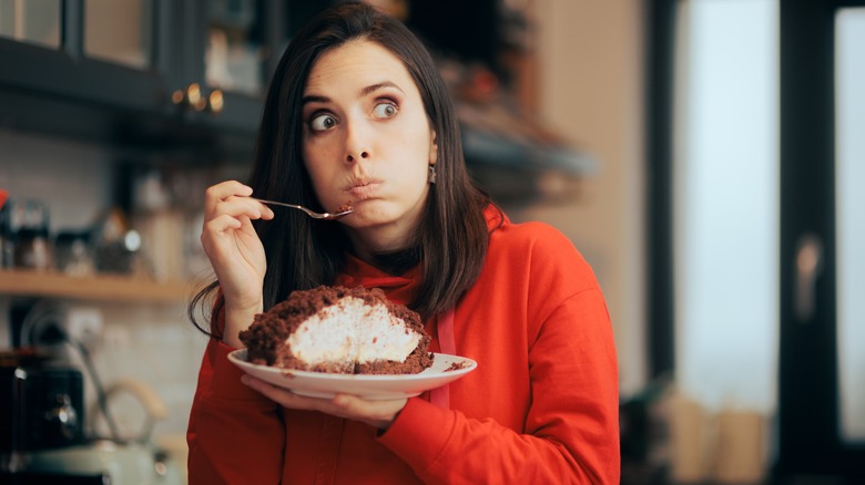 Woman eating cake with guilty expression