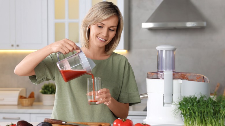 Smiling woman pouring a glass of tomato juice