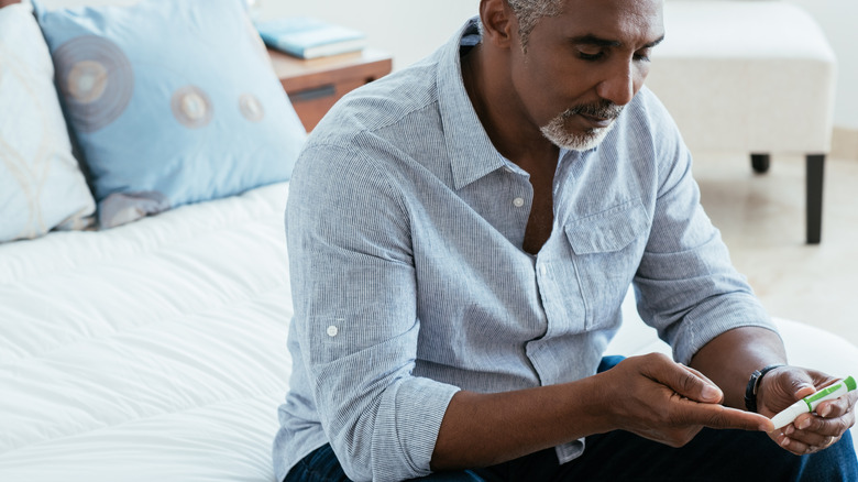 Man sitting on a be checking his blood sugar levels